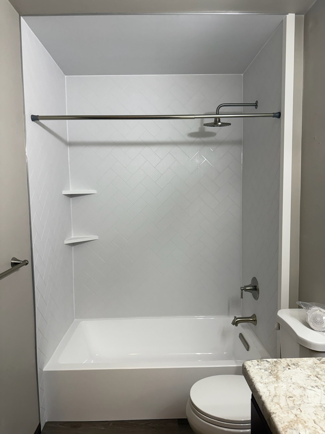 Bathtub replacement with a white alcove bathtub, white herringbone textured walls, a brushed nickel rain shower head and tub spout and corner shelves in Hobart, WI