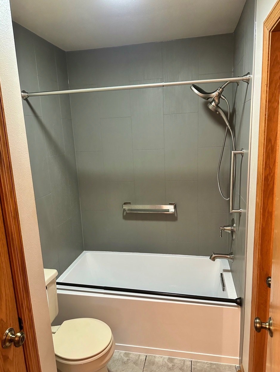 Bathtub replacement with a white bathtub, smooth grey walls, a brushed nickel handheld shower on a slide bar, a grab bar and a curtain rod in a Wisconsin home
