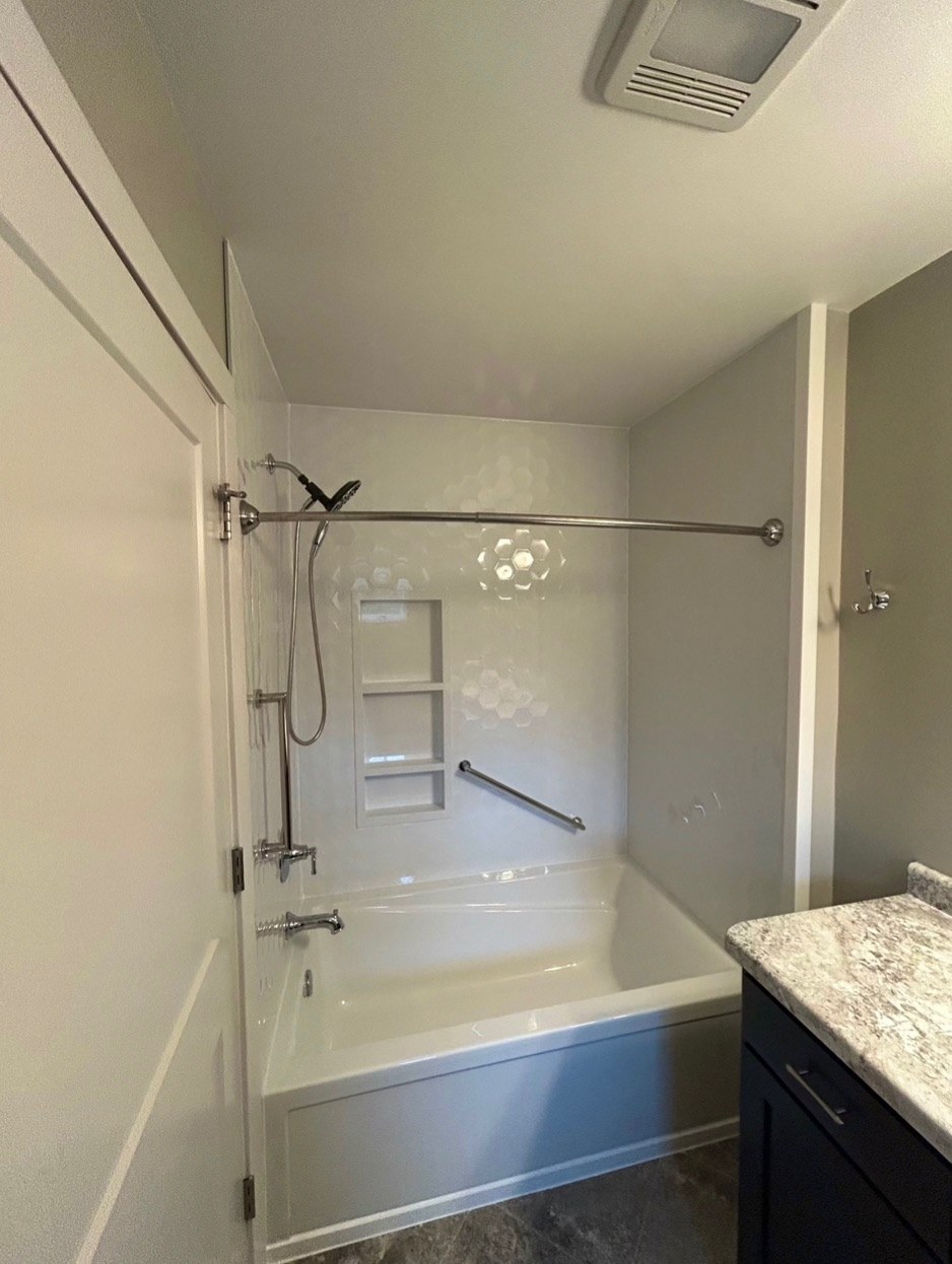 Bathtub replacement with a white bathtub, Samuel Mueller Gloss White Hexagon walls, a brushed nickel handheld shower on a slide bar, a three shelf recessed niche and a grab bar in a Wisconsin home
