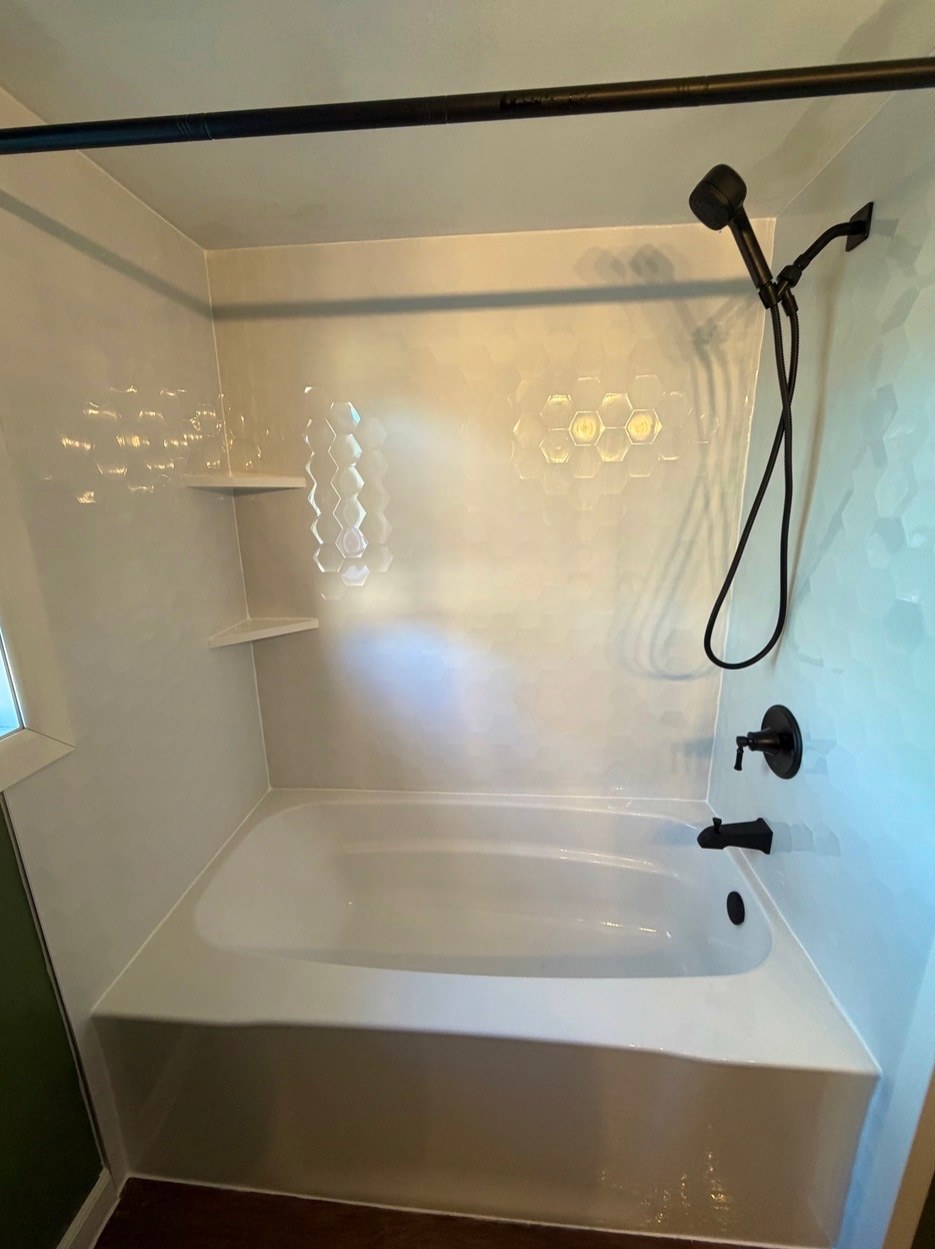 Bathtub replacement with a white bathtub, Samuel Mueller Gloss White Hexagon walls, a matte black handheld shower on a slide bar, a matte black tub spout and corner shelves in a Wisconsin home