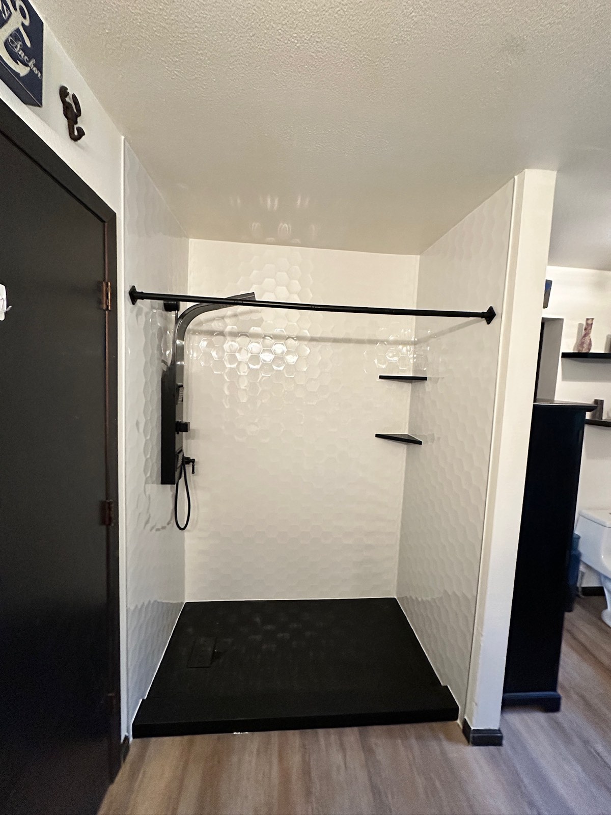 Low threshold shower with Samuel Mueller Gloss White Hexagon walls, a matte black shower panel with a handheld sprayer, black corner shelves and a black shower base in Grand Rapids, WI