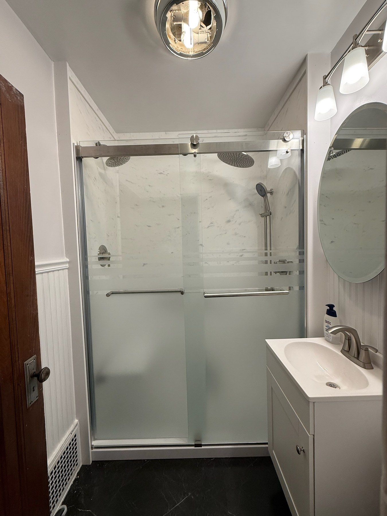 Shower replacement with white marble look walls, a frosted sliding glass door, two brushed nickel rain shower heads and a handheld on a slide bar in Oshkosh, WI