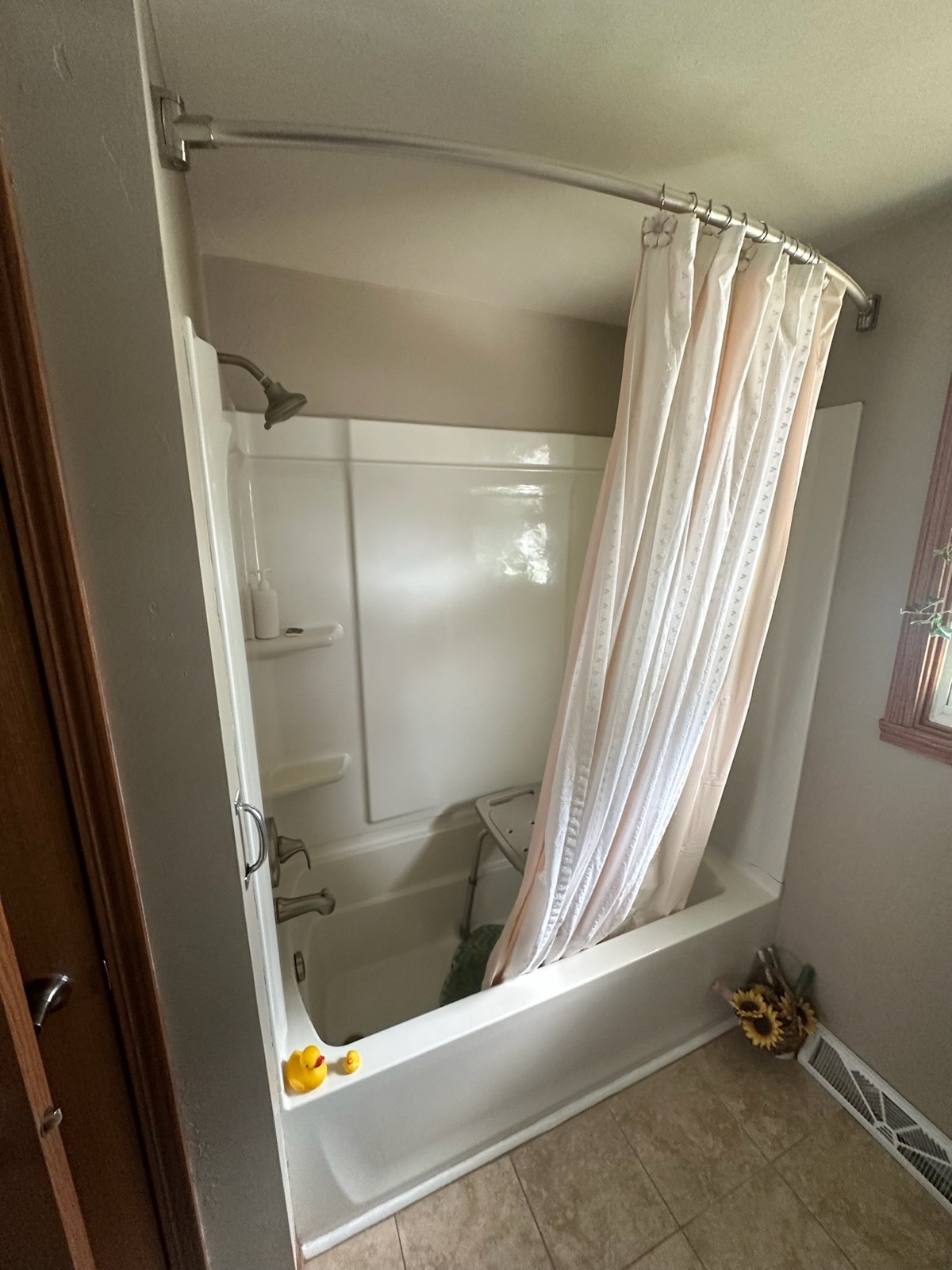 Before: the original alcove bathtub with a shower curtain and a shower chair in a Bellevue, WI bathroom
