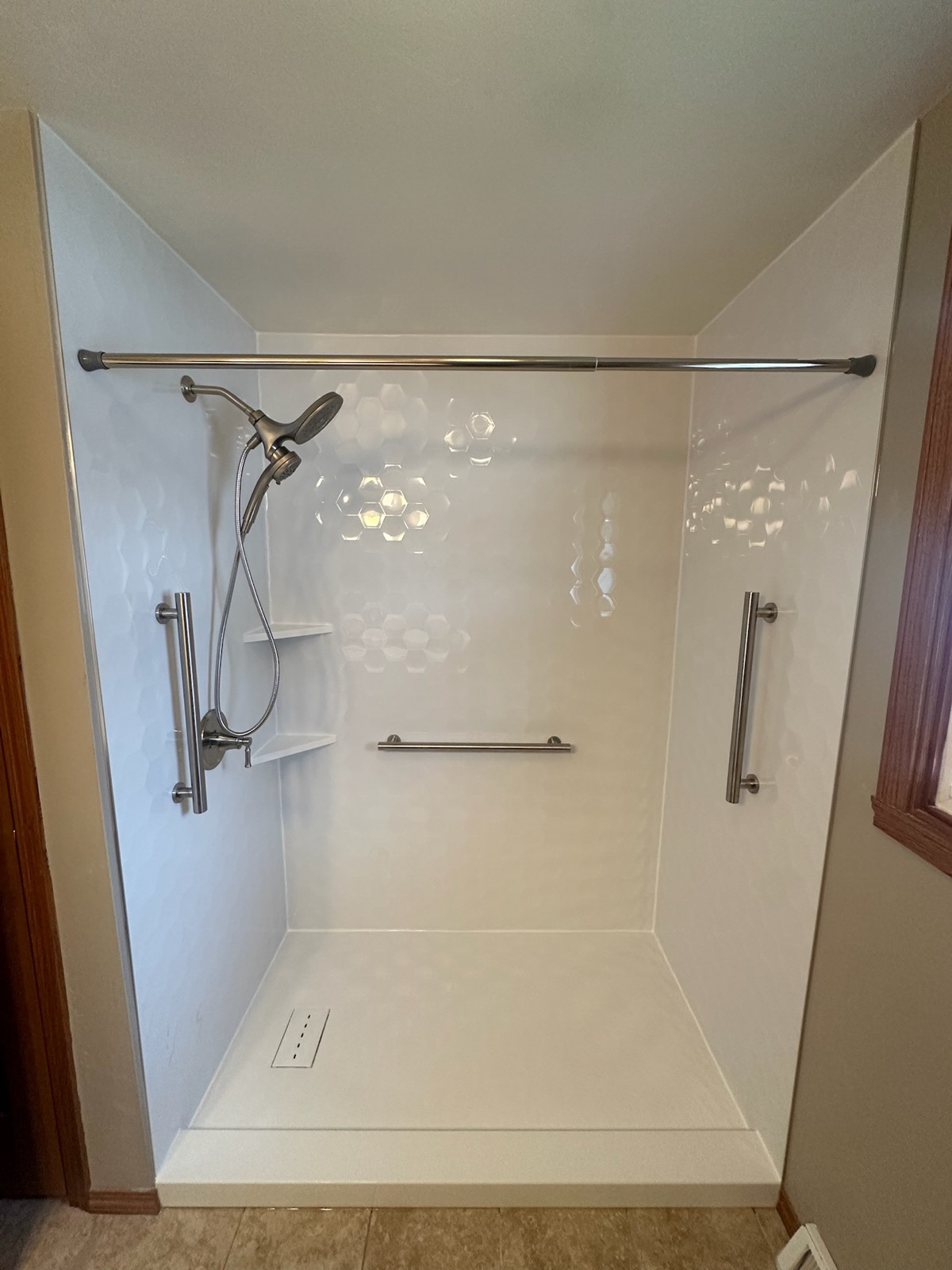 Tub to shower conversion with Samuel Mueller Gloss White Hexagon walls, a brushed nickel handheld shower on a slide bar, three grab bars, corner shelves and a low threshold base in Bellevue, WI