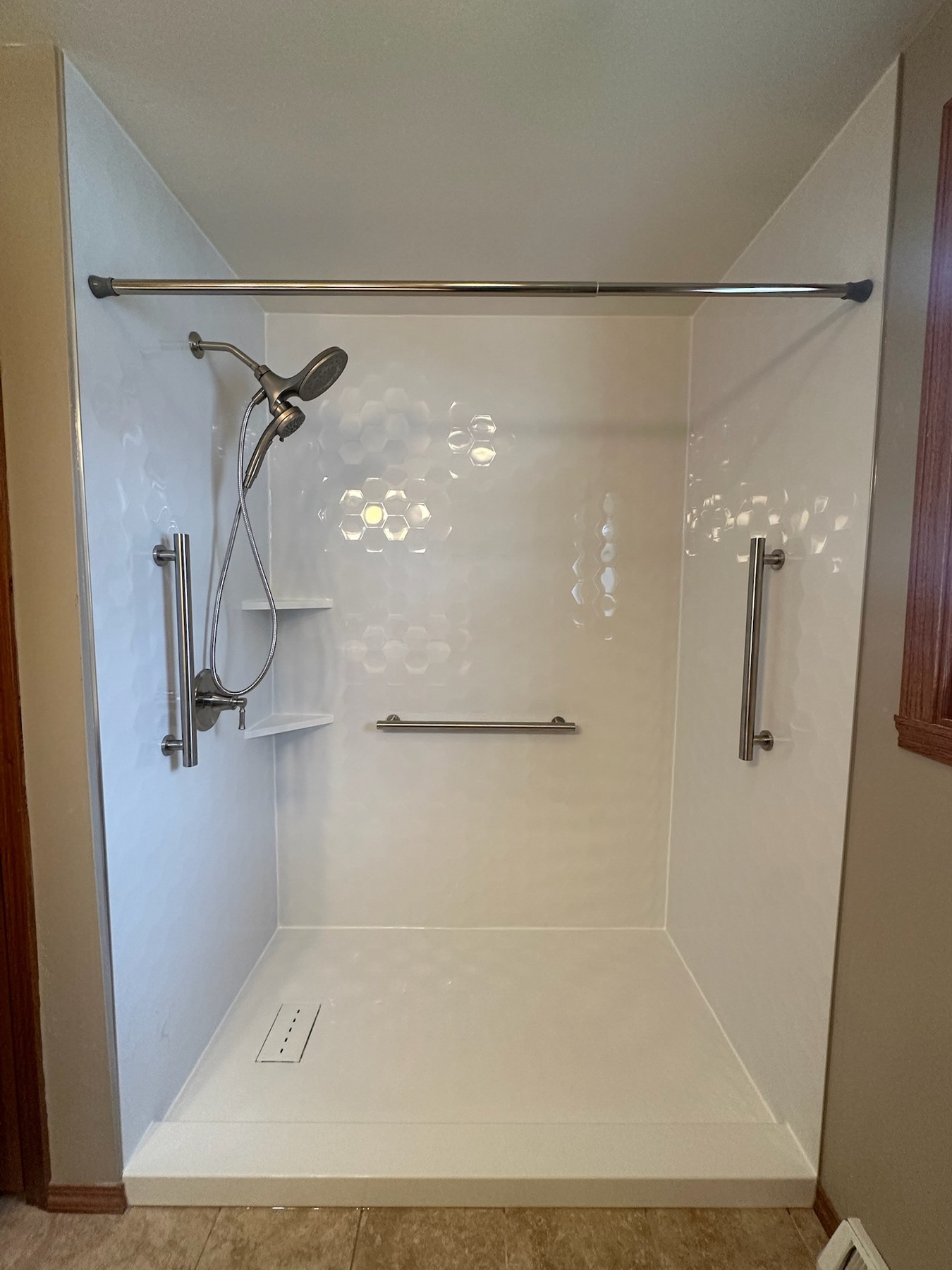 Tub to shower conversion with Samuel Mueller Gloss White Hexagon walls, brushed nickel grab bars on three walls, a handheld shower on a slide bar, corner shelves and a low threshold base in Bellevue, WI