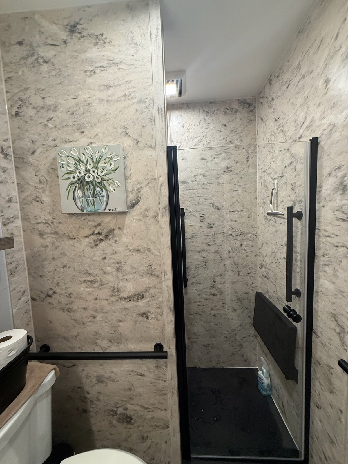 Marble look walls from floor to ceiling around a black framed glass shower door with a black fold down seat and black grab bars in Appleton, WI