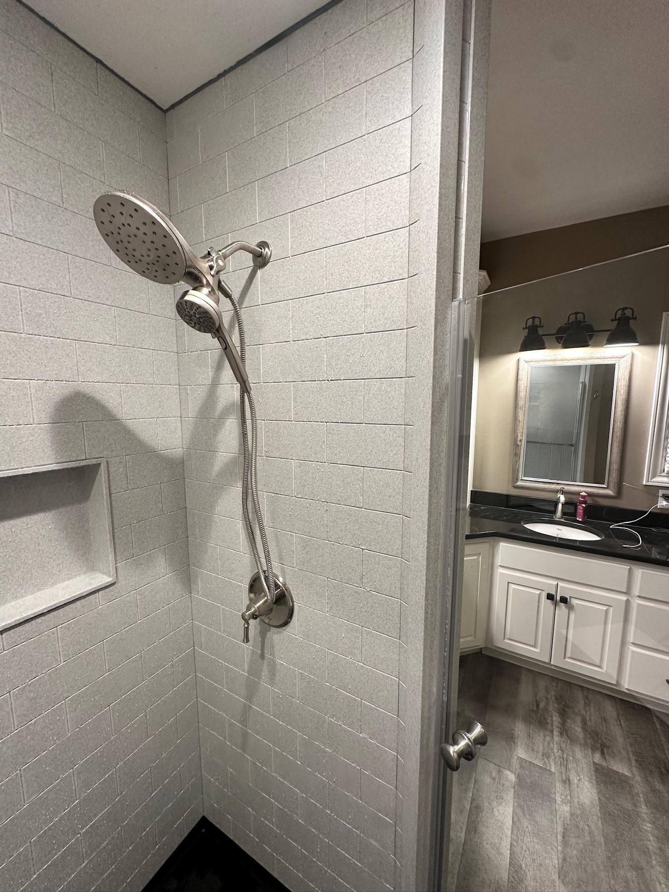 Detail of a brushed nickel rain shower head and handheld with a recessed niche against grey textured subway look walls in Howard, WI