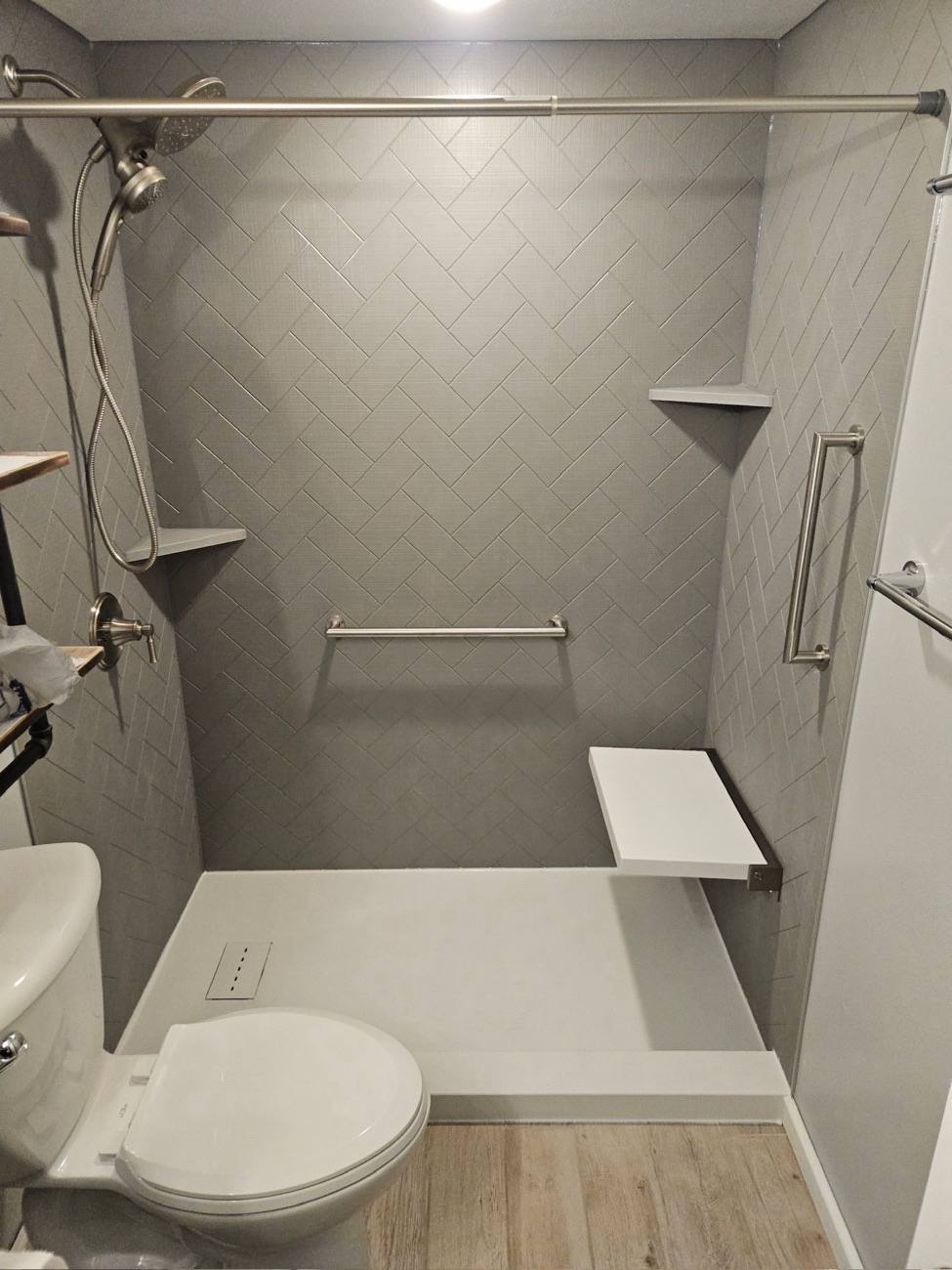 Grey solid surface shower with a fold down seat and grab bars installed by American Shower Company