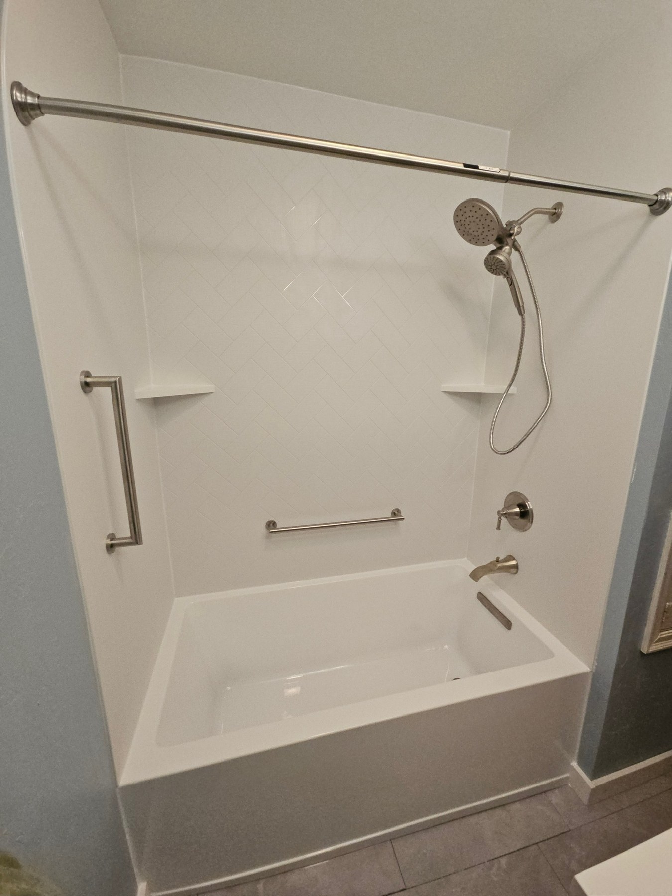 White alcove bathtub with smooth white walls, a brushed nickel handheld shower on a slide bar, grab bars and corner shelves installed by American Shower Company in a Wisconsin home