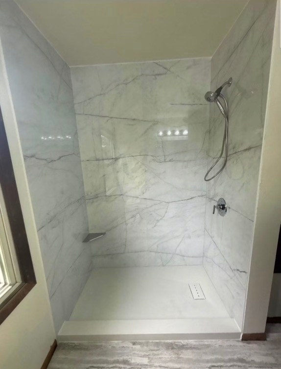 Shower with white and grey veined marble look walls, a brushed nickel handheld shower on a slide bar, a corner shelf and a white base installed by American Shower Company in a Wisconsin home