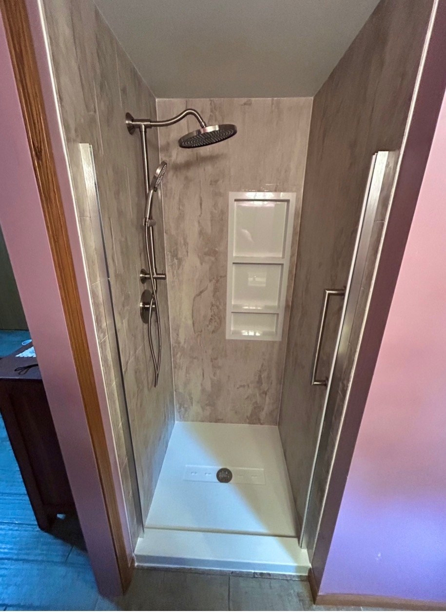 Shower with tan stone look walls, a brushed nickel rain shower head and handheld on a slide bar, a three shelf recessed niche and a white base installed by American Shower Company in a Wisconsin home