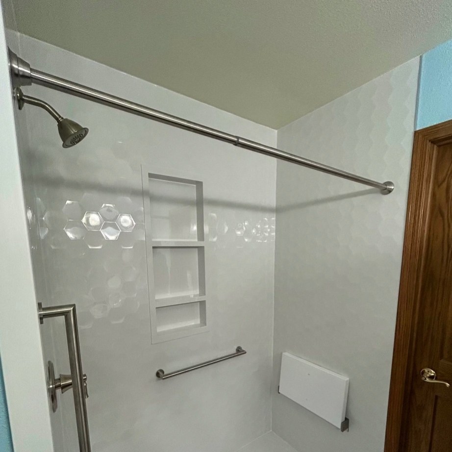 Walk in shower with Samuel Mueller Gloss White Hexagon walls, a brushed nickel rain shower head, a three shelf recessed niche, grab bars, a white fold down seat and a white low threshold base installed by American Shower Company in a Wisconsin home