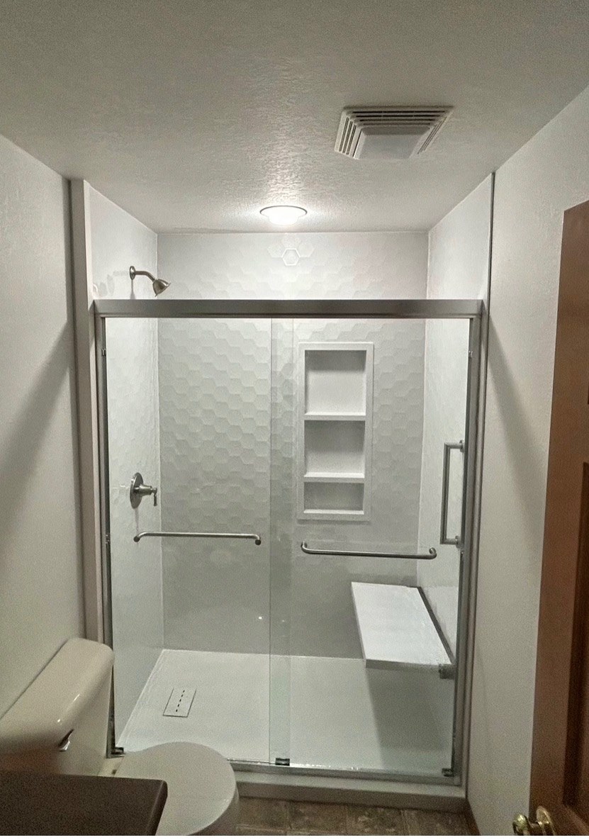 Walk in shower with Samuel Mueller Gloss White Hexagon walls, a chrome framed sliding glass door, a recessed niche, grab bars and a white fold down seat installed by American Shower Company in a Wisconsin home